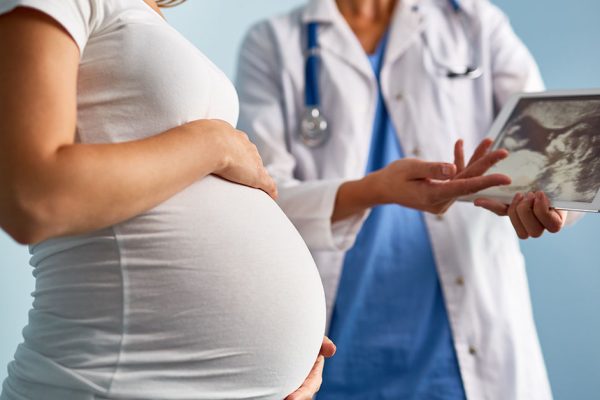 Mid-section image of unrecognizable female doctor explaining ultrasound scan results to pregnant woman using digital tablet